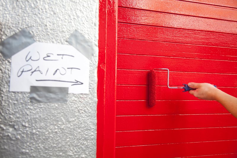 Work in progress of a fresh coat of siren red paint on an outdoor garage door in San Jose, CA